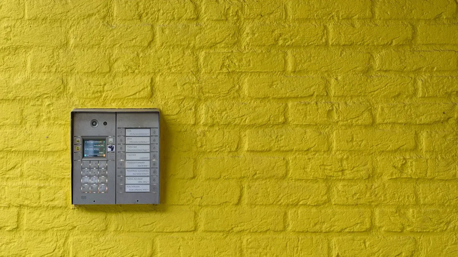 A vibrant yellow brick wall featuring a modern intercom system, ideal for security or design concepts.