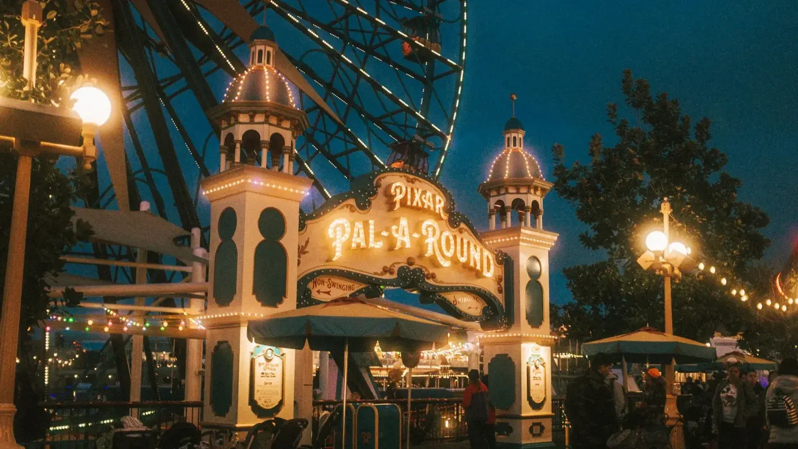 The iconic entrance of the Pixar Pal-A-Round ferris wheel illuminated at night in a vibrant amusement park setting.