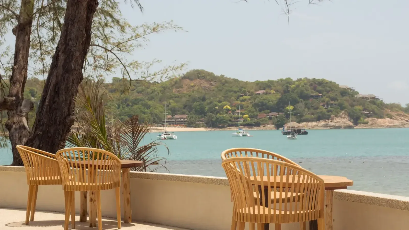 Serena terraza junto al mar con sillas de madera con vistas a una tranquila bahía, típica de un relajante resort de verano.