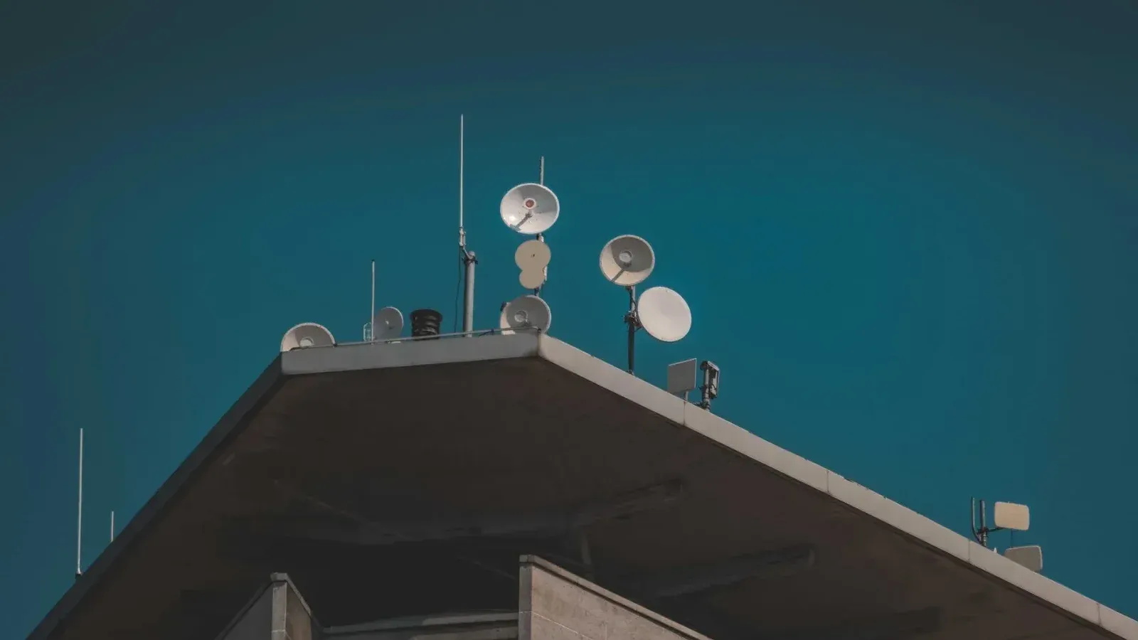 Una vista de ángulo bajo de platos de comunicación y antenas en un edificio contra un cielo azul claro.