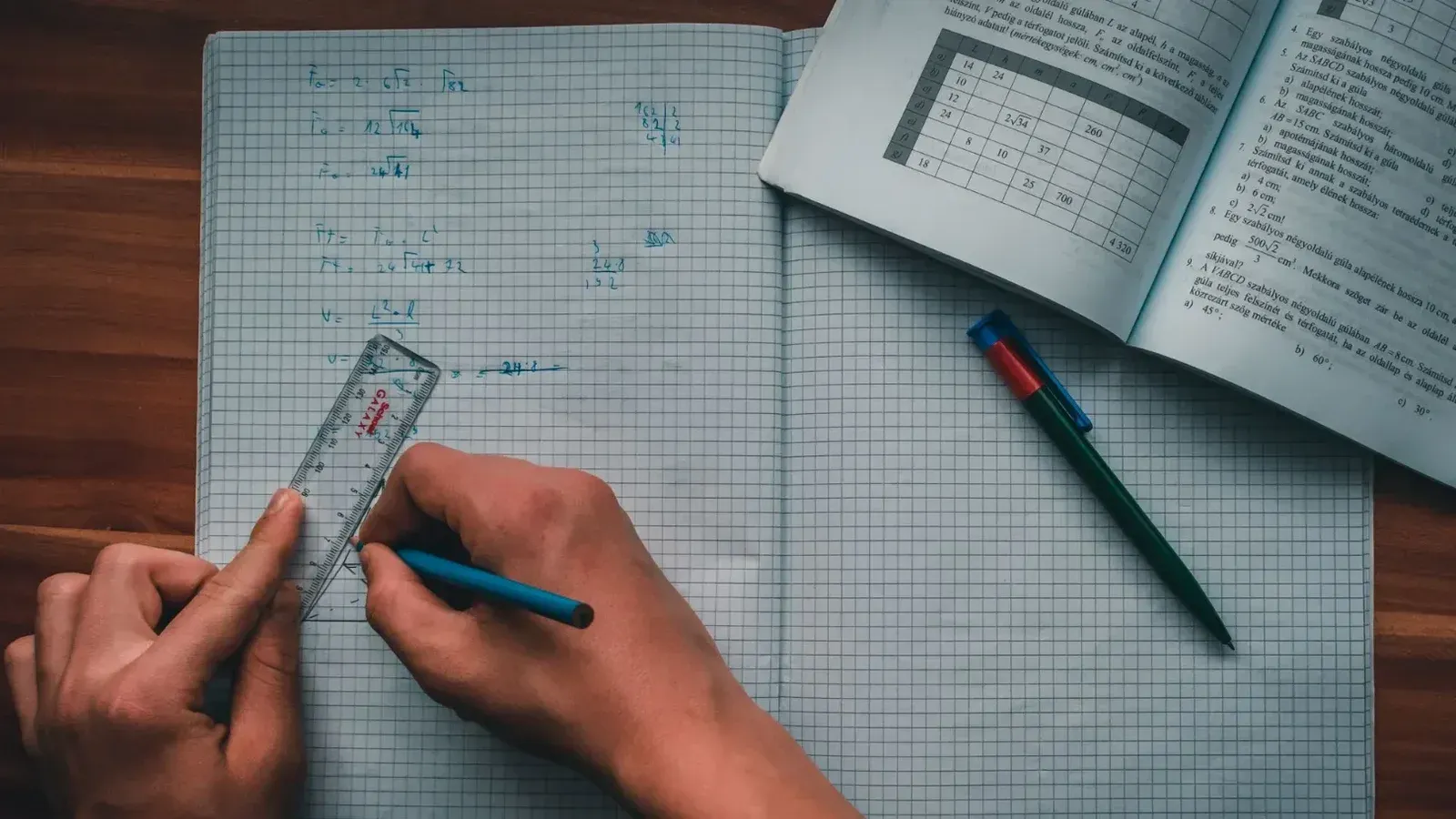 Una persona escribe ecuaciones matemáticas en un cuaderno usando una regla y un lápiz, enfocados en resolver problemas.