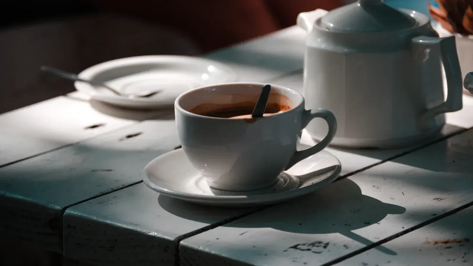 Taza de café blanco y olla sobre una mesa bañada por el sol, creando un ambiente acogedor.