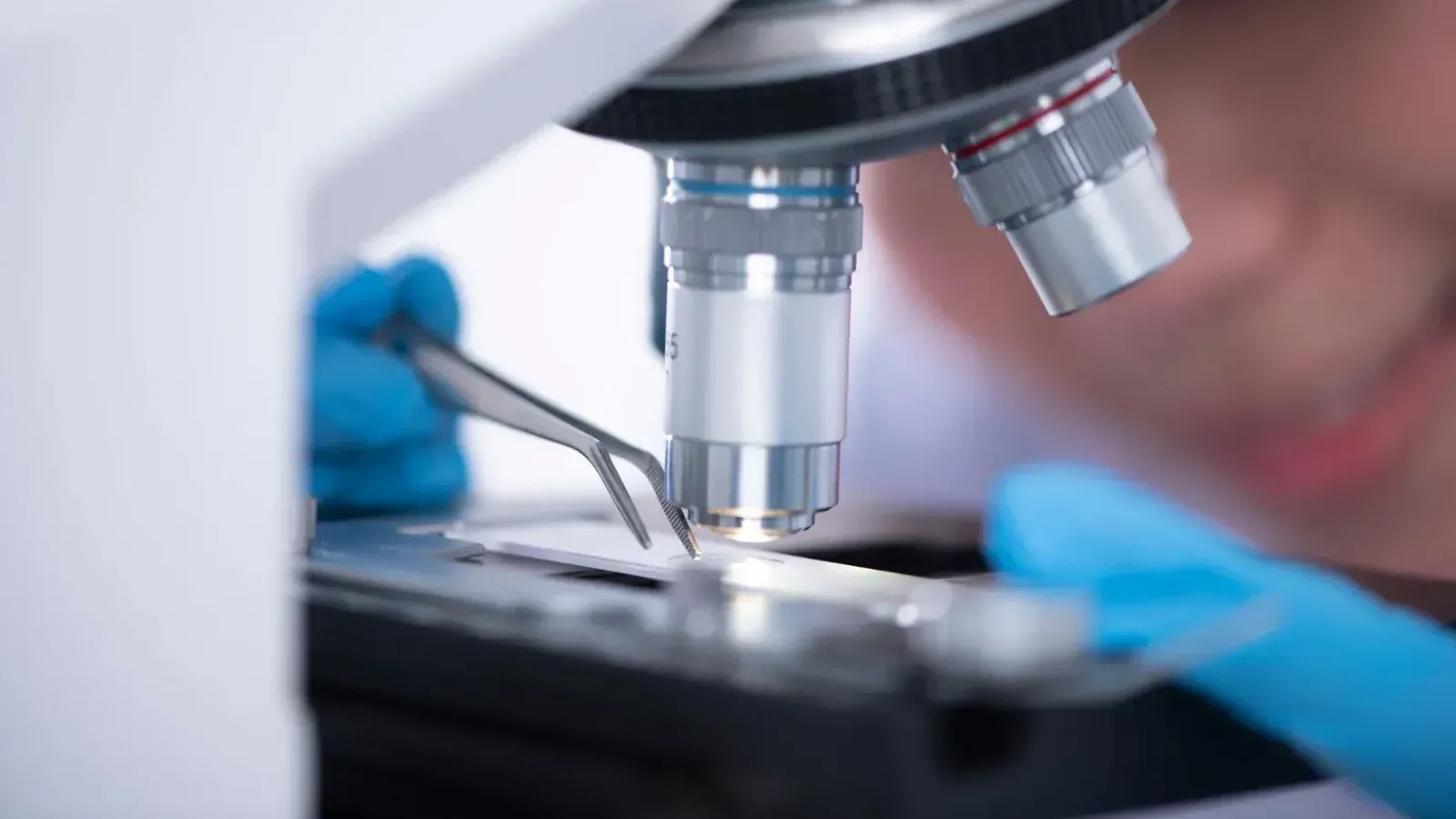 Blurred unrecognizable person placing sample on microscope while making research during work in modern laboratory