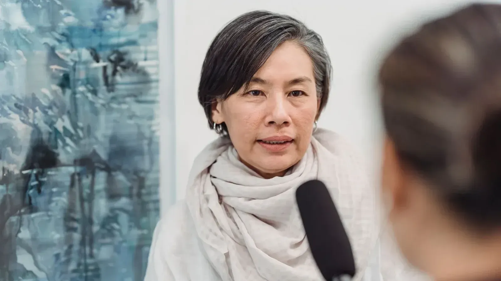 Mujer asiática en discusión con un periodista en una galería de arte interior.