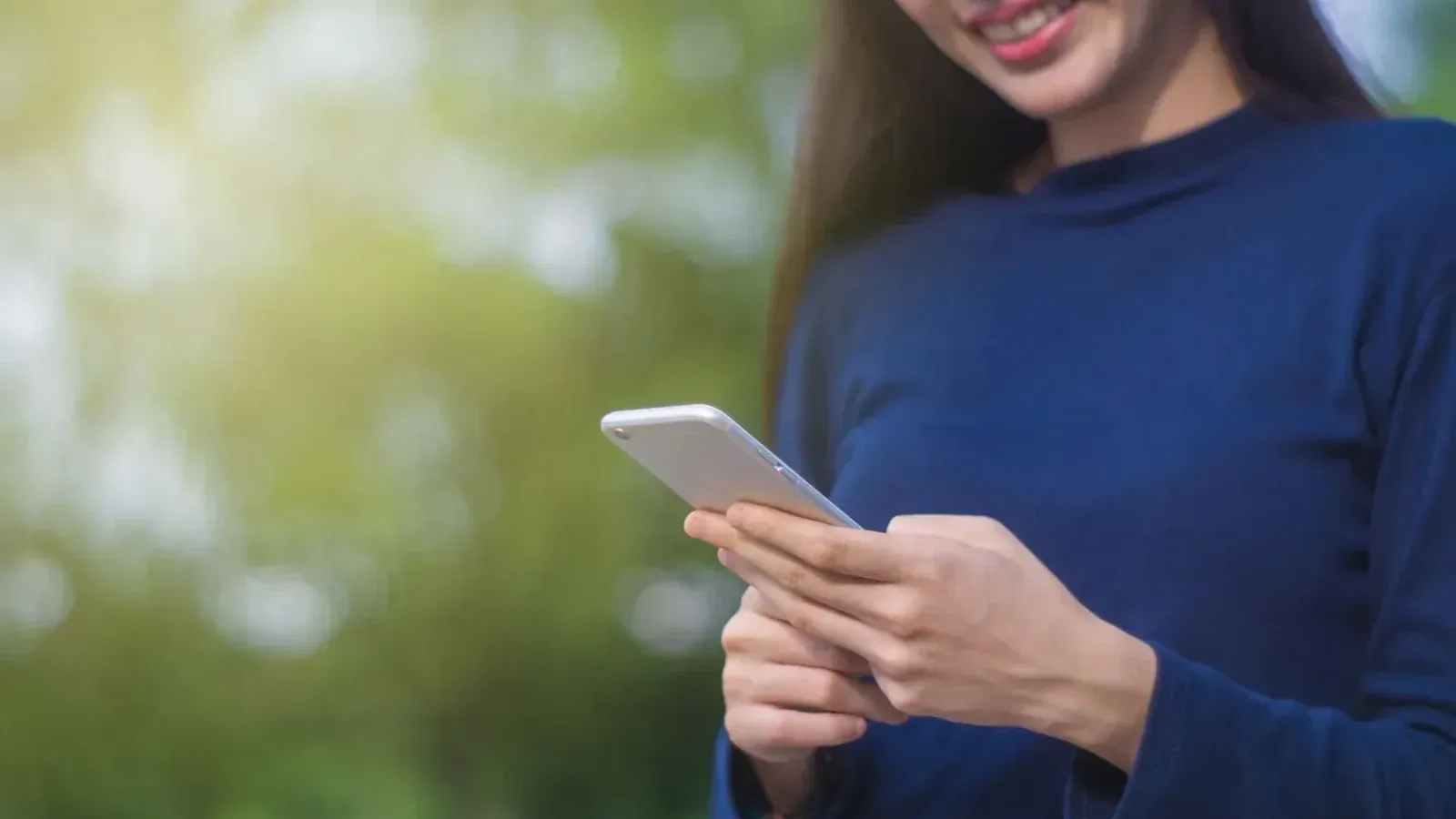 A woman using a smartphone outdoors, conveying positive emotions and modern technology in nature.