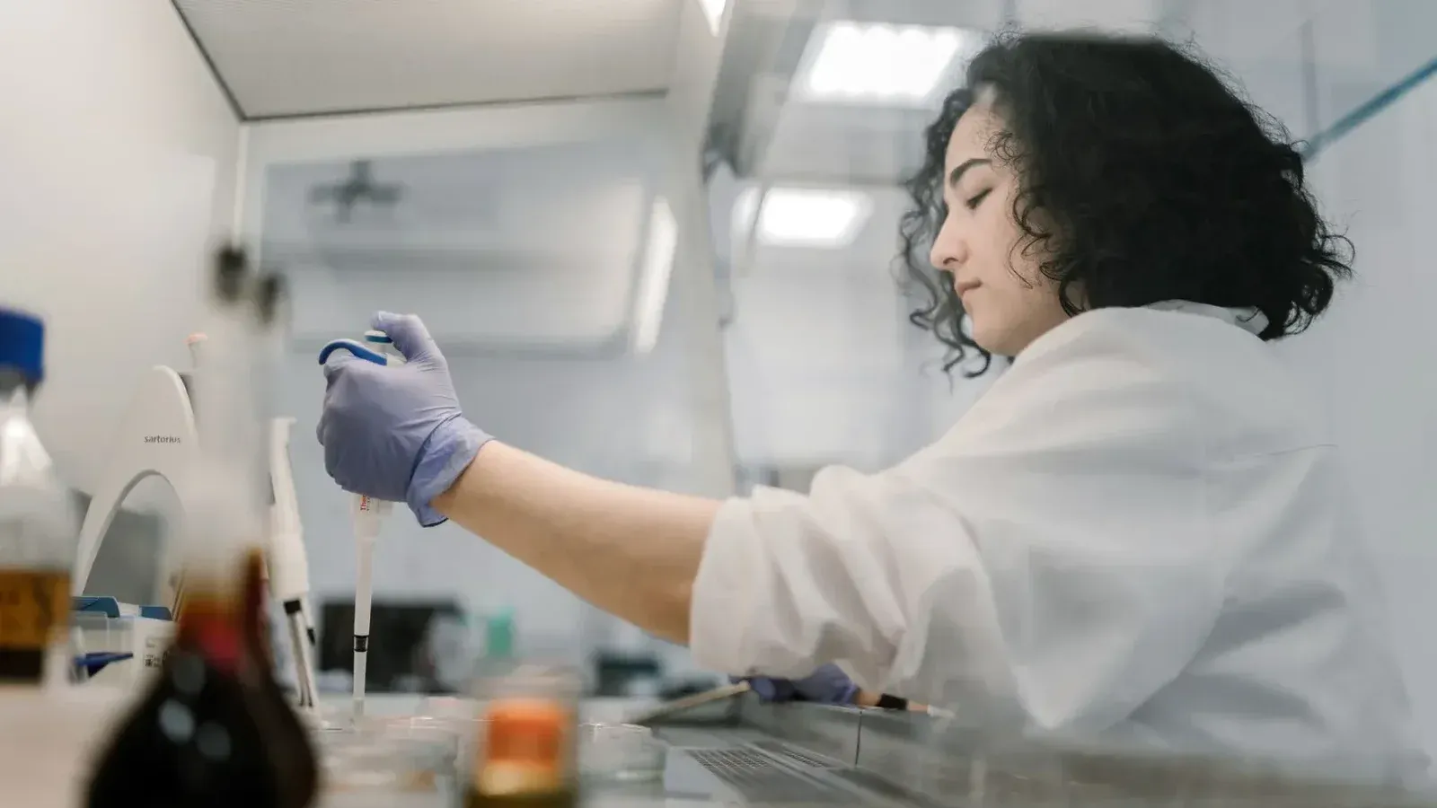 Mujer en bata de laboratorio realizando investigaciones con pipeta en laboratorio moderno.