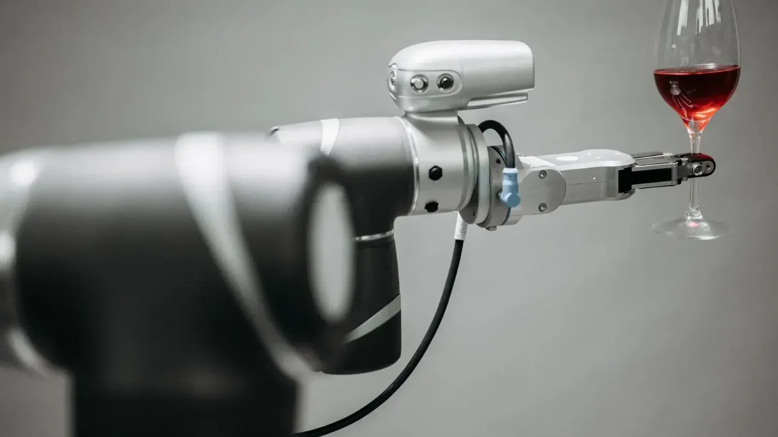 Un brazo robótico sosteniendo cuidadosamente una copa de vino tinto contra un fondo neutral, mostrando la innovación.