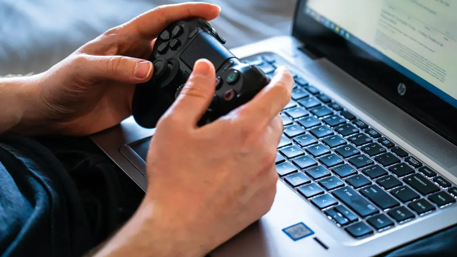 Person holds a gaming controller while interacting with a laptop, emphasizing modern gaming technology.