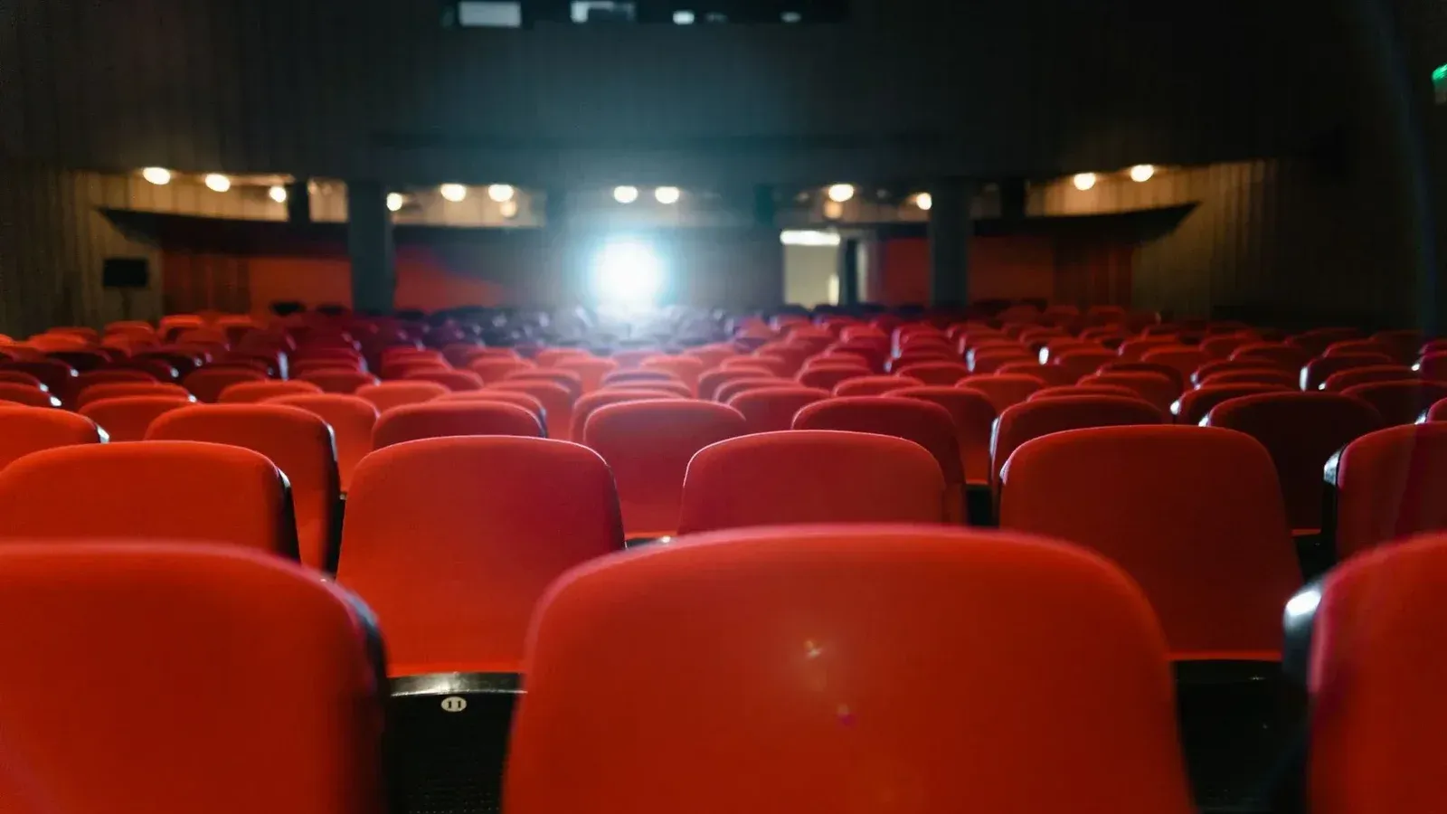 Una vista de un cine vacío con filas de asientos rojos frente a la pantalla iluminada.