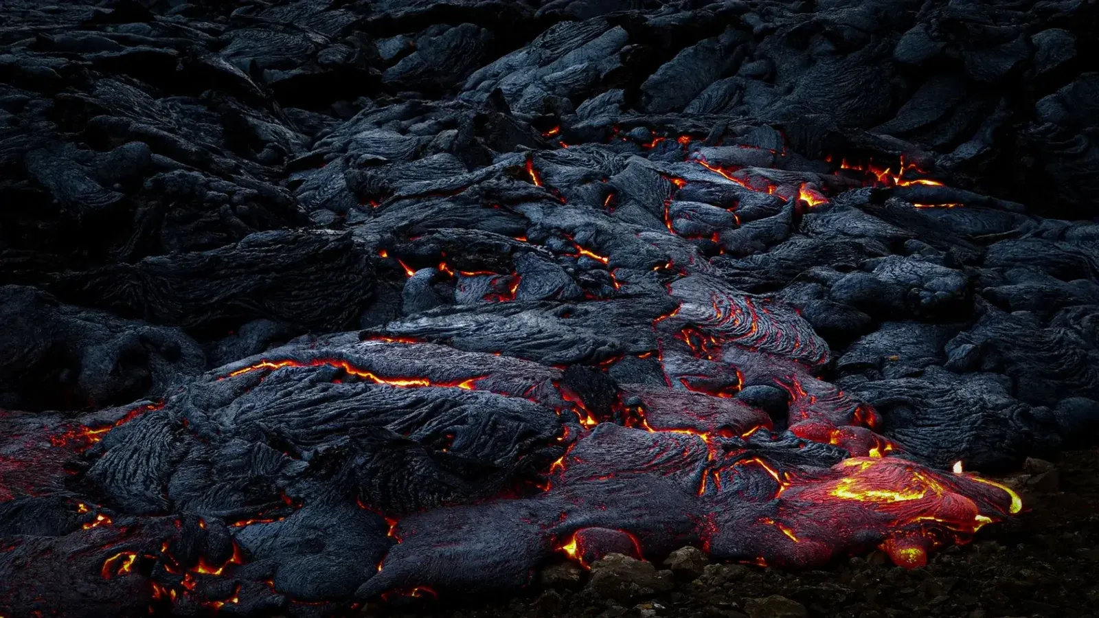 Primer plano de lava vívida y fundida que fluye sobre rocas volcánicas oscuras y refrigeradas por la noche.