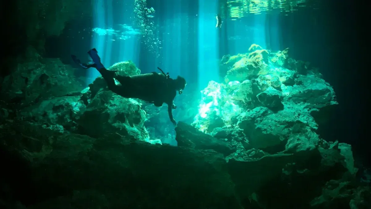 Scuba diver explores serene underwater coral formations illuminated by natural light rays.