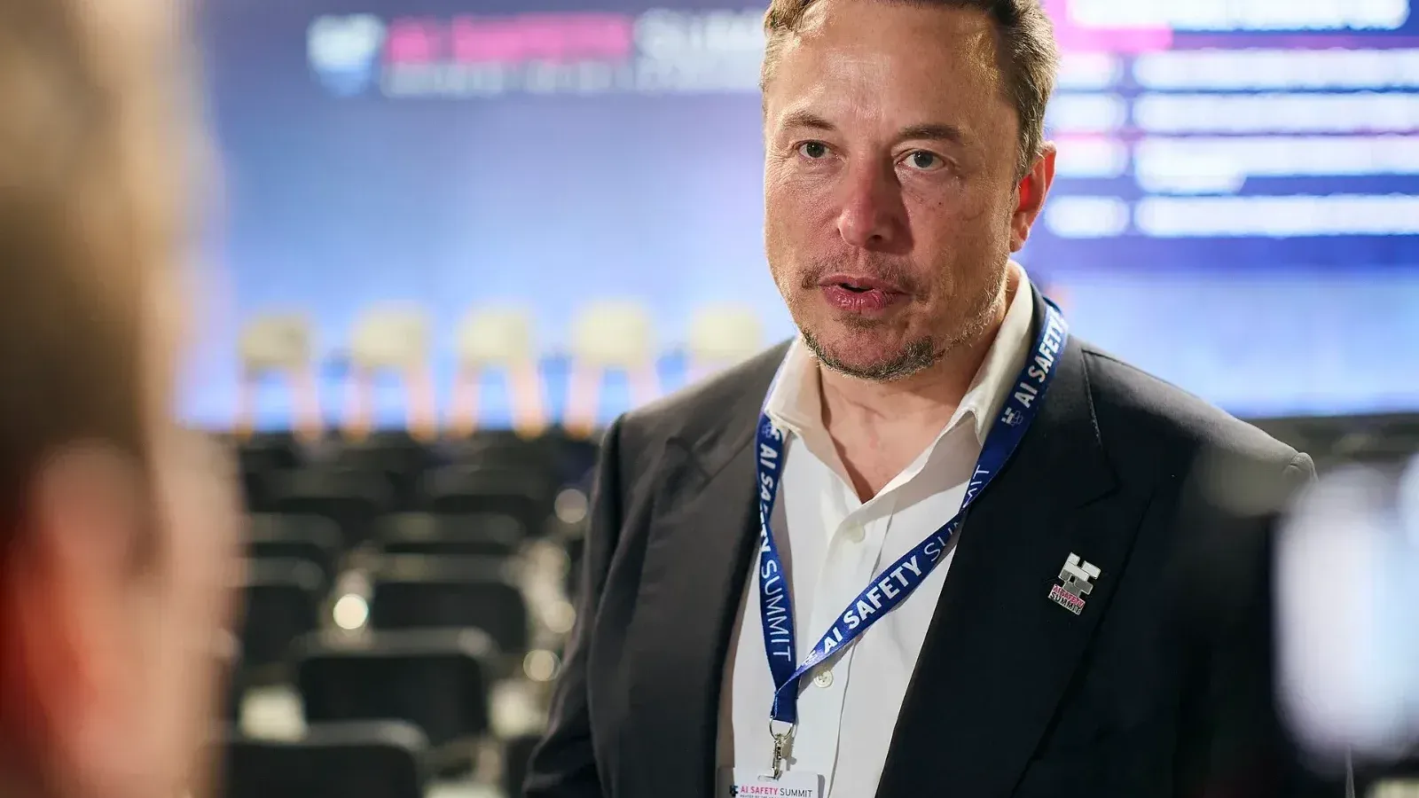 Elon Musk, con traje oscuro y credencial de la Cumbre de Seguridad de la IA al cuello, habla en la sala del encuentro en Bletchley Park, Reino Unido