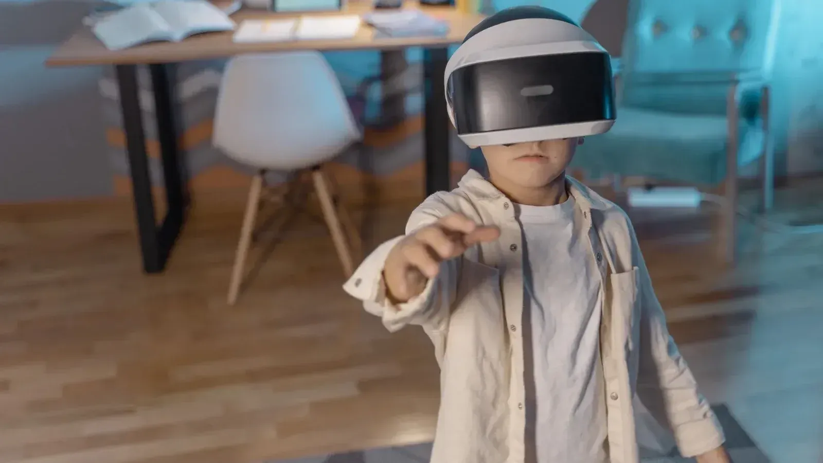 Joven lleva gafas de realidad virtual, explorando la realidad virtual en interiores con libros abiertos en el escritorio cerca.