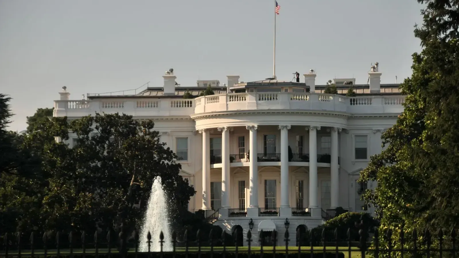 La majestuosa casa blanca con su arquitectura icónica rodeada de exuberante vegetación, con una majestuosa fuente.