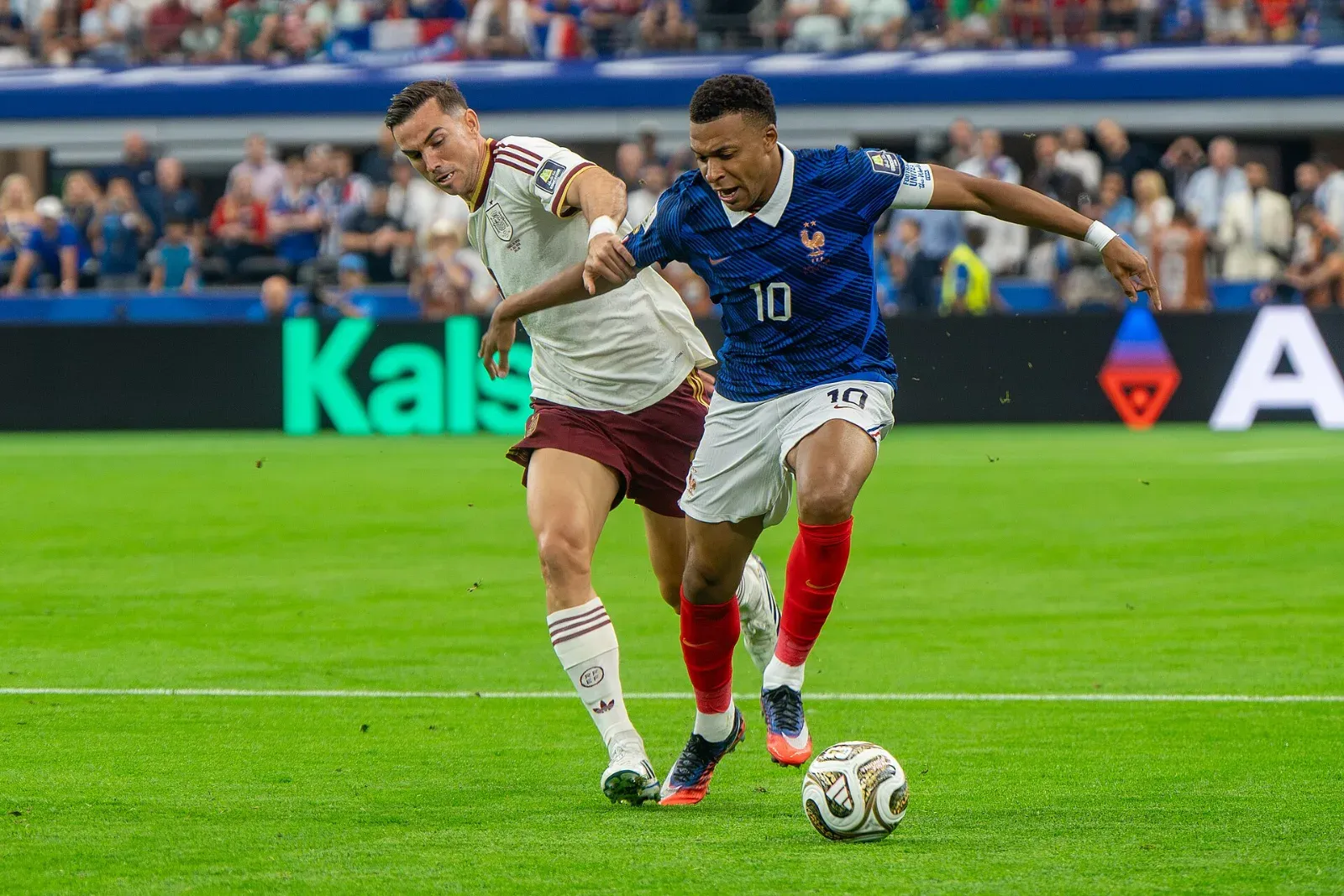 Kylian Mbappé, con la camiseta azul número 10 de Francia, conduce el balón mientras Fabián Ruiz, de blanco y granate, lo marca de cerca.