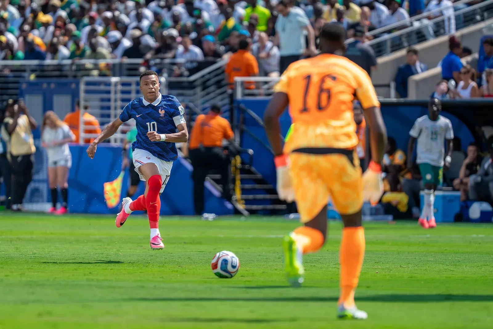 Kylian Mbappé, con la camiseta azul y el dorsal 10 de Francia, conduce el balón hacia el portero de Senegal, de naranja con el número 16.