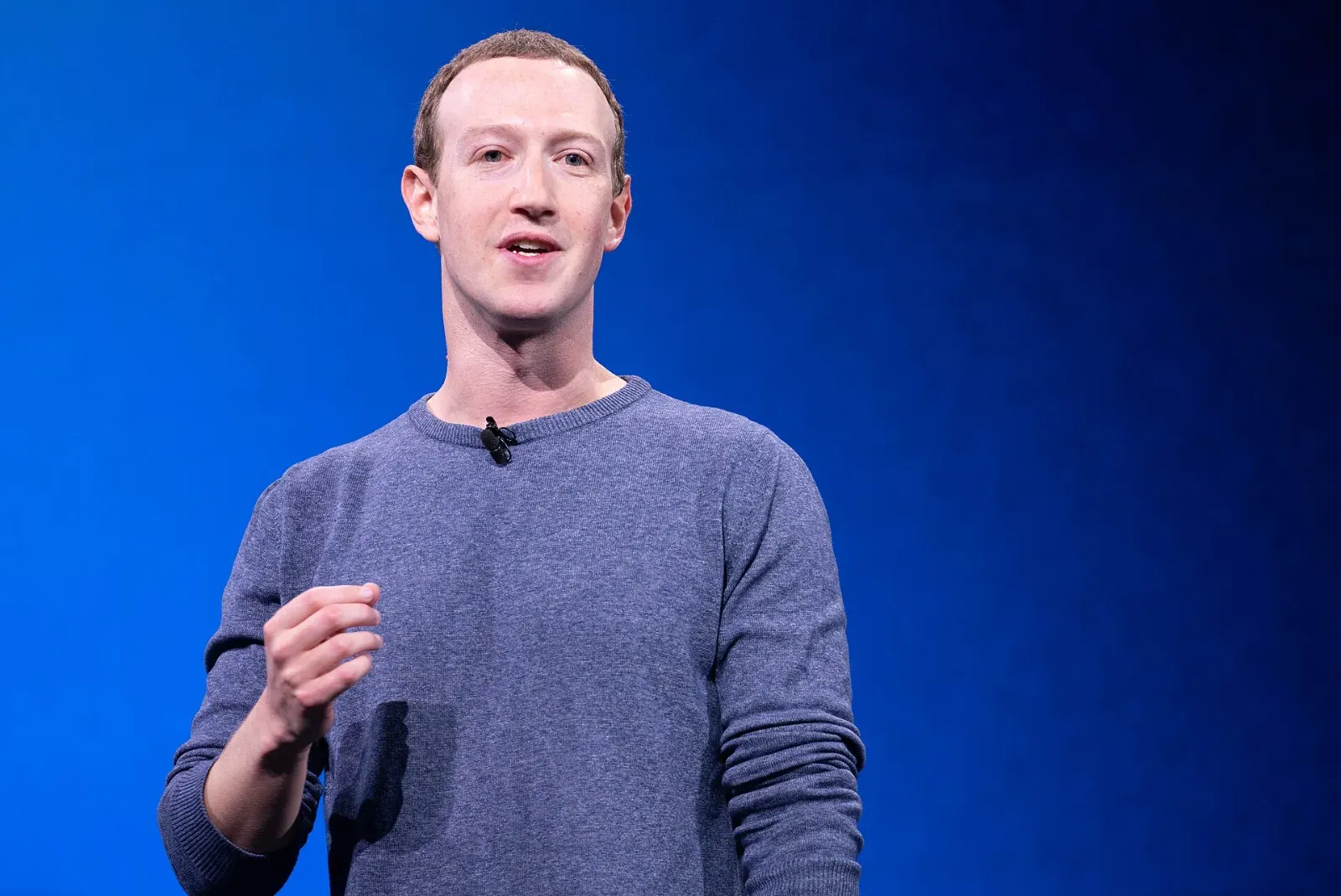 Mark Zuckerberg, con suéter azul grisáceo y micrófono de solapa, habla de pie frente a un fondo azul durante una conferencia.