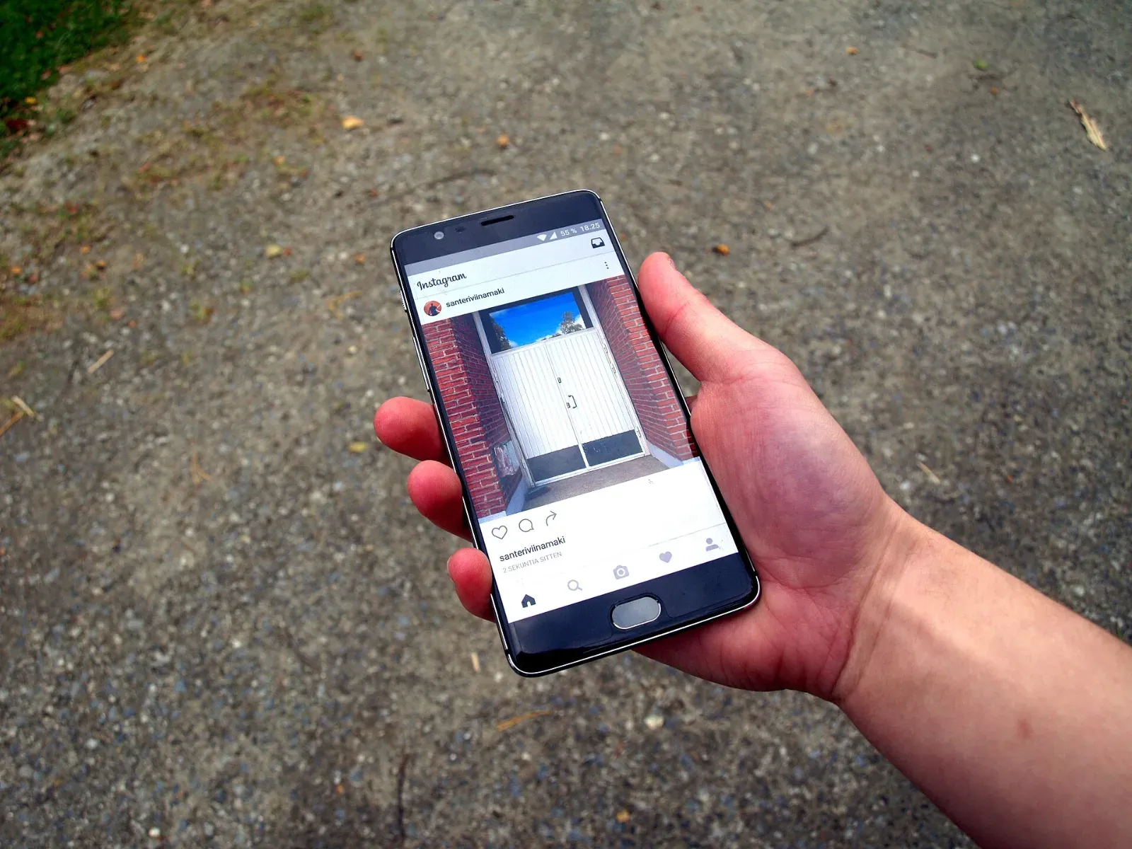 Una mano sostiene un teléfono inteligente con la aplicación de Instagram abierta en la pantalla, sobre un suelo de asfalto.