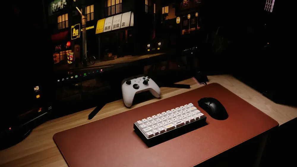 Primer plano de una configuración de escritorio de juegos con teclado, controlador y monitor por la noche.