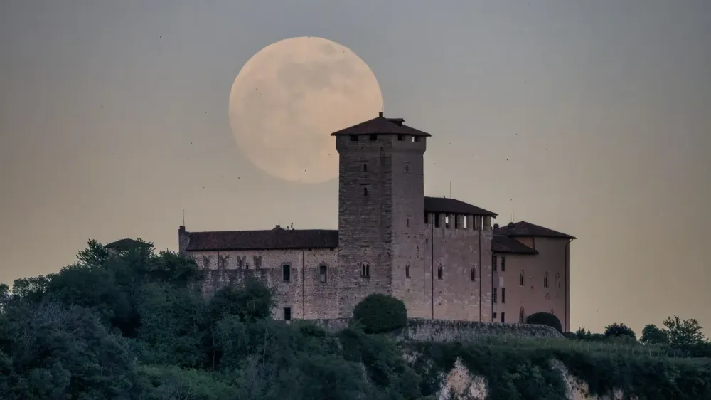 Silhouette of a medieval castle against a backdrop of a full moon at twilight.