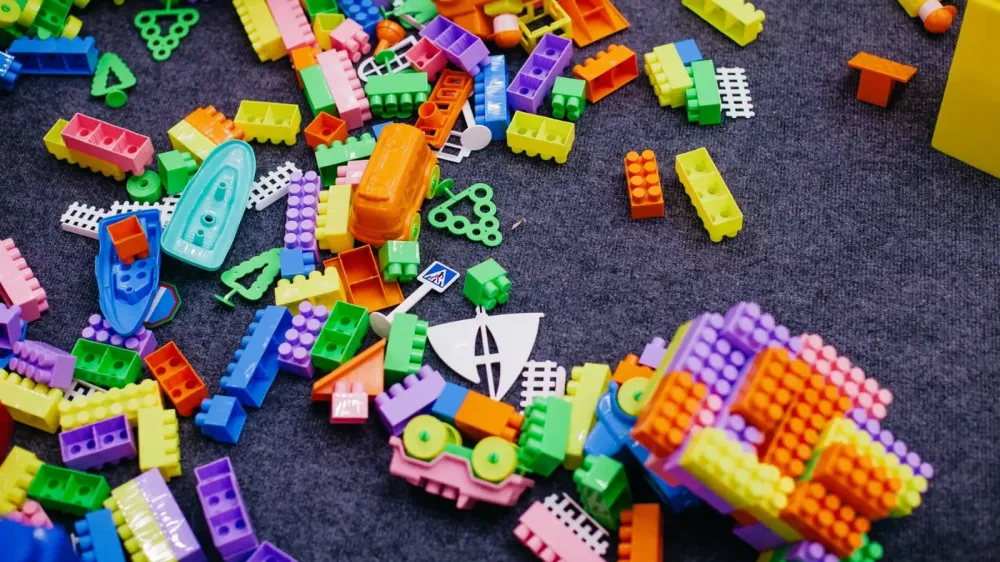 Vibrant plastic toy blocks scattered on a grey carpet, showcasing assorted shapes and colors.