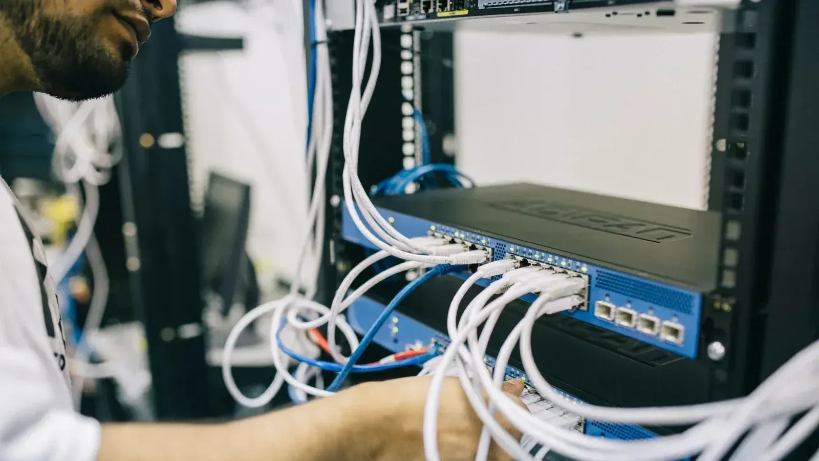 Un profesional de TI configurando cables de red en un rack de servidores, centrándose en las conexiones Ethernet.