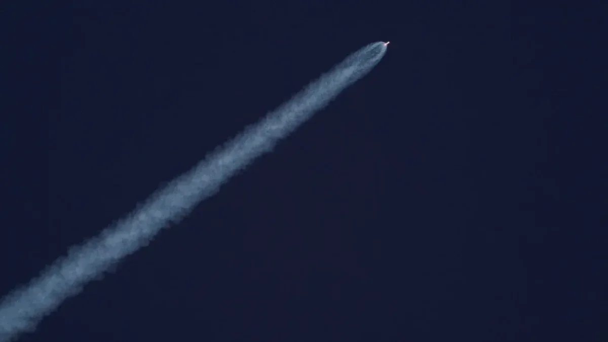 Un cohete asciende hacia el cielo, dejando un rastro de humo contra el cielo azul claro.