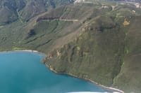 A stunning aerial view of a green mountain range beside a serene coastline.