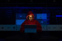 Focused woman in a red hoodie using a laptop in a dimly lit room with technology brands displayed.