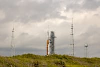 NASA rocket on launch pad surrounded by antennas against a cloudy sky.