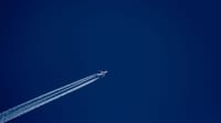 A high-flying airplane leaves distinct contrails against a clear blue sky, capturing the essence of flight.