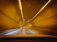 Blurry traffic scene with cars speeding through a brightly lit tunnel at night.