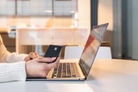 A woman using a credit card and laptop for online shopping in a modern indoor setting.