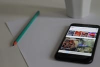 Smartphone displaying news, next to pencil and paper on a desk, showcasing modern technology in a workspace.