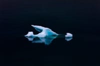 A serene scene of a floating iceberg with reflection on calm ocean waters during winter.
