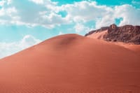 Stunning red sand dunes under a bright blue sky with clouds, creating a dramatic desert landscape.