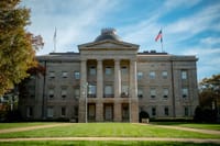 Front view of the historic North Carolina State Capitol in Raleigh, showcasing neoclassical architecture under a blue sky.
