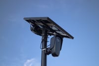 Solar-powered surveillance camera with a clear blue sky backdrop, highlighting modern technology.