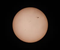 A detailed photograph of the sun highlighting visible sunspots against a dark background.