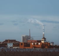 Factory with smokestack emitting smoke under a clear sky, industrial setting.