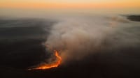 Dramatic aerial shot of a forest fire spreading with smoke at sunset in South Africa.
