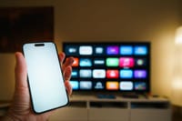 A smartphone in focus with a smart TV displaying apps in a cozy living room.