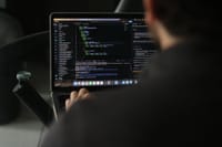 A focused developer writing code on a laptop in an indoor workspace.