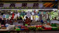 Bustling Asian market stall with vendor selling fresh produce and vegetables.