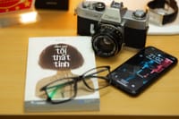 Close-up of a vintage camera with a book and smartphone on a wooden desk.