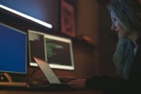 Woman working on cybersecurity programming with laptops and multiple screens