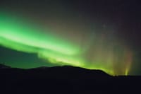 From below picturesque view of colorful shiny polar lights illuminating sky over mount silhouette at dusk