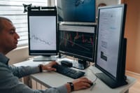 A professional in an office analyzing financial charts on multiple monitors, using advanced technology.