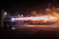A powerful rocket engine test firing with vibrant flames illuminating the night sky.