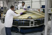 Concentrated male mechanics in protective uniform assembling detail of large spacecraft component at modern factory